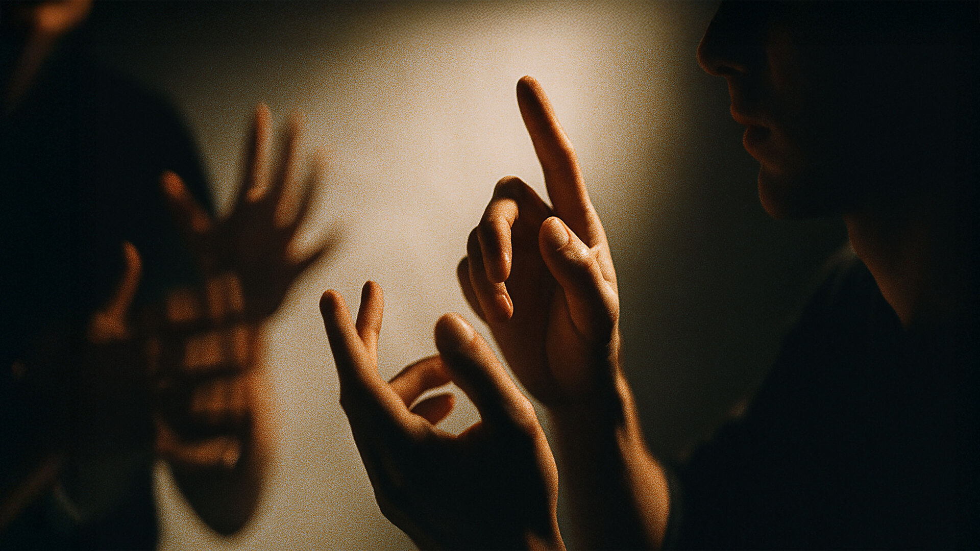 Zwei Personen im Dunkeln, deren Hände Licht reflektieren und Zeichensprache gestikulieren.