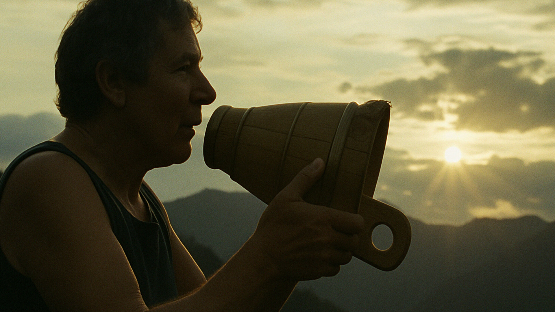 Silhouette einer Person mit Megafon vor untergehender Sonne in den Bergen.