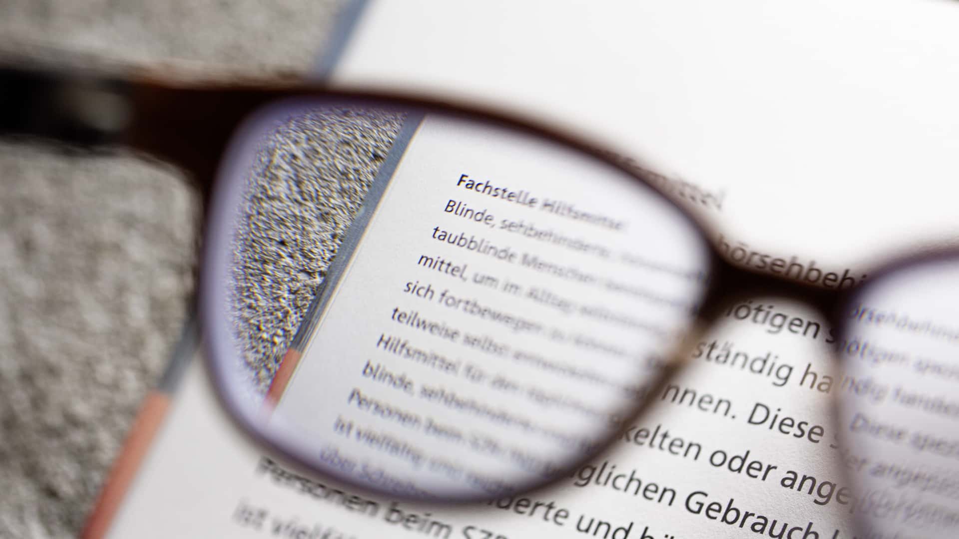Brille liegt auf einem Buch, der Text ist durch das Glas vergrössert sichtbar.