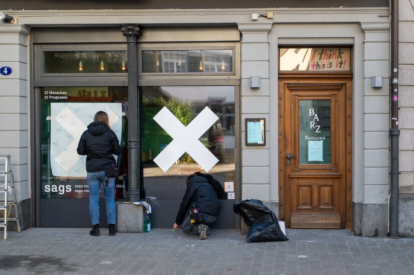 Zwei Personen gestalten die Schaufensterfront eines Geschäfts mit grossen weissen Kreuzen und dem Logo der Agentur sags.